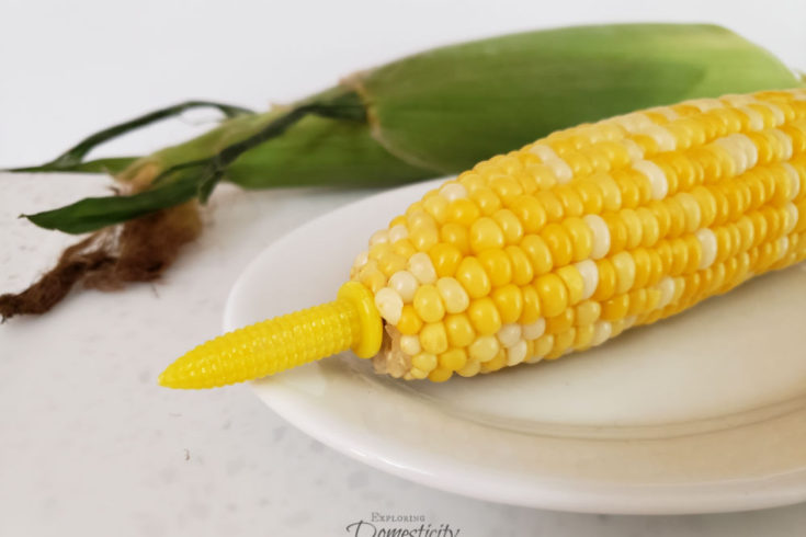 no-peel microwave corn-on-the-cob with corn holders in front of an unshucked ear of corn