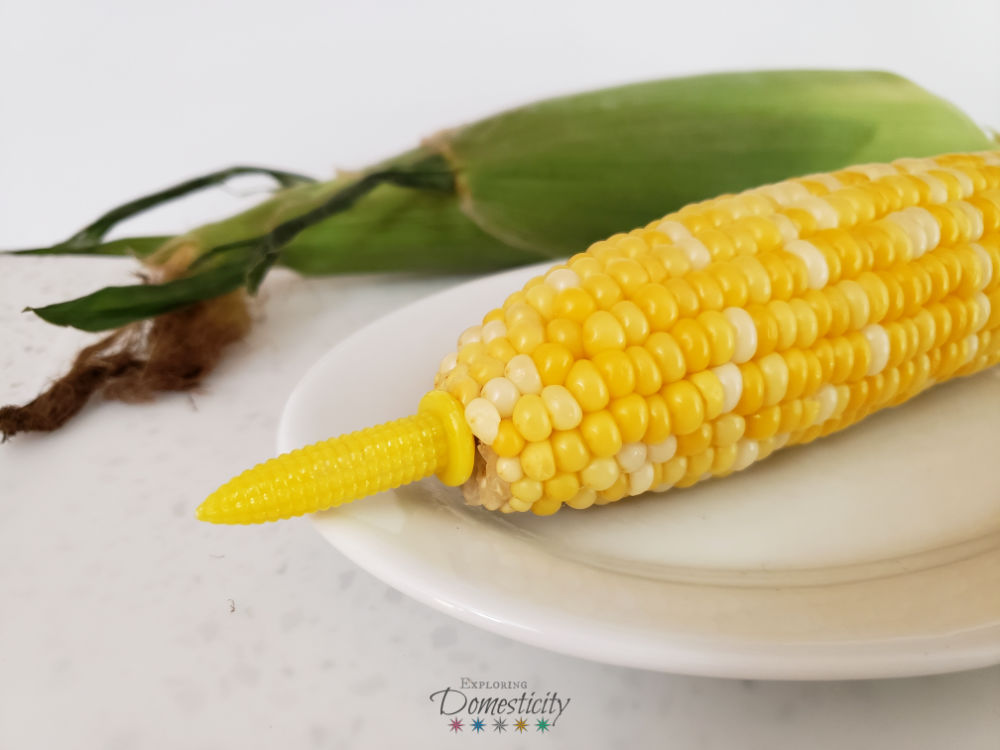 no-peel microwave corn-on-the-cob with corn holders in front of an unshucked ear of corn