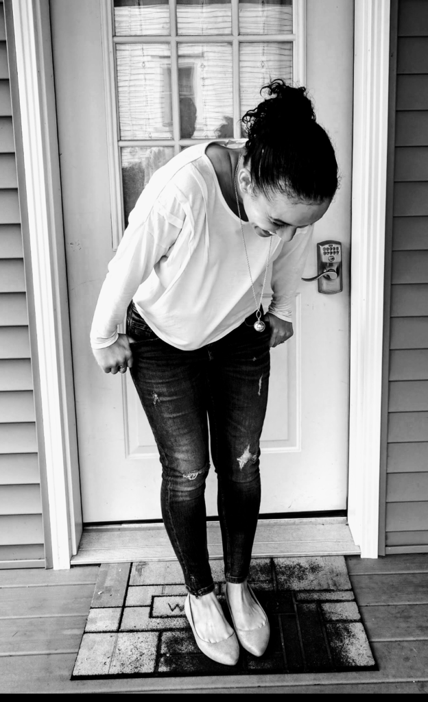 Sheree in front of a door, laughing and looking down at her feet. The photo is in black and white