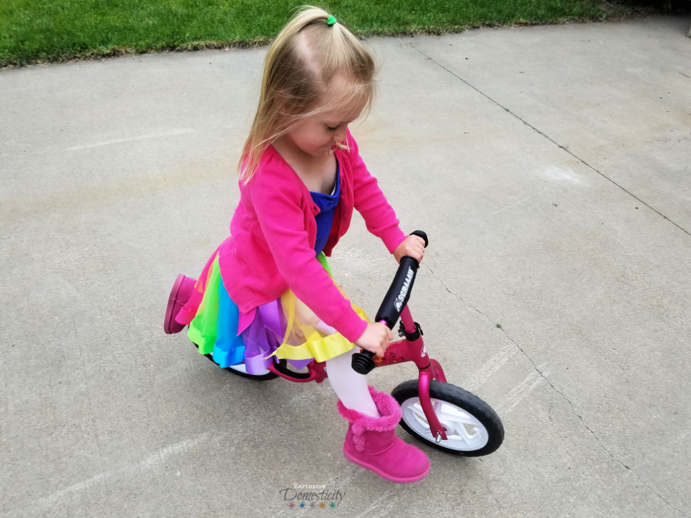girl in rainbow tutu on a pink balance bike