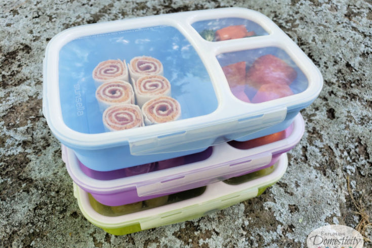 Stack of three colorful bento boxes with pinwheel sandwiches for school lunch