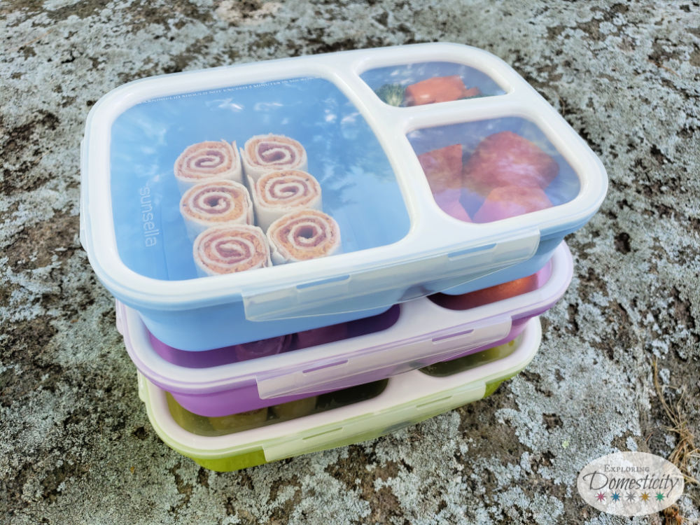 Stack of three colorful bento boxes with pinwheel sandwiches for school lunch