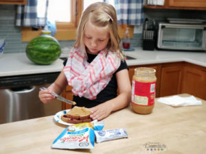 Little Girl in kitchen making peanut butter and jelly sandwich with veggie straws and snack bar