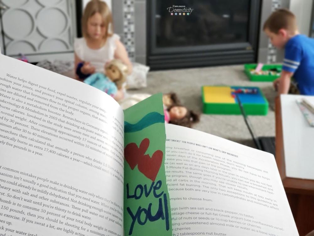 Reading book with I Love You bookmark while kids play