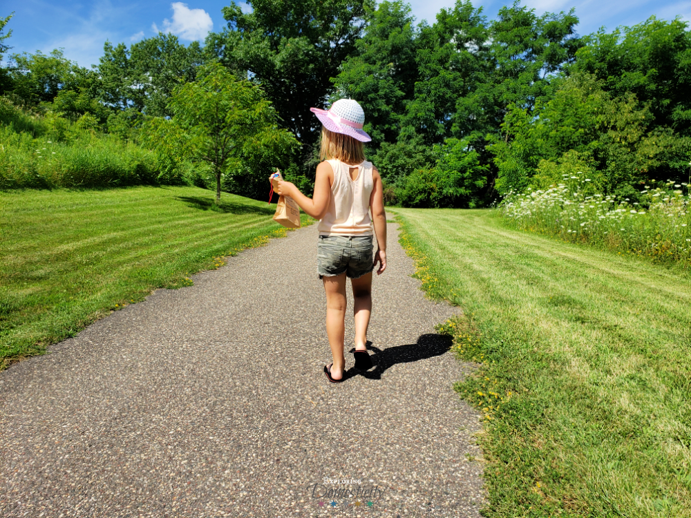 girl in hat walking on path with scavenger hunt bag